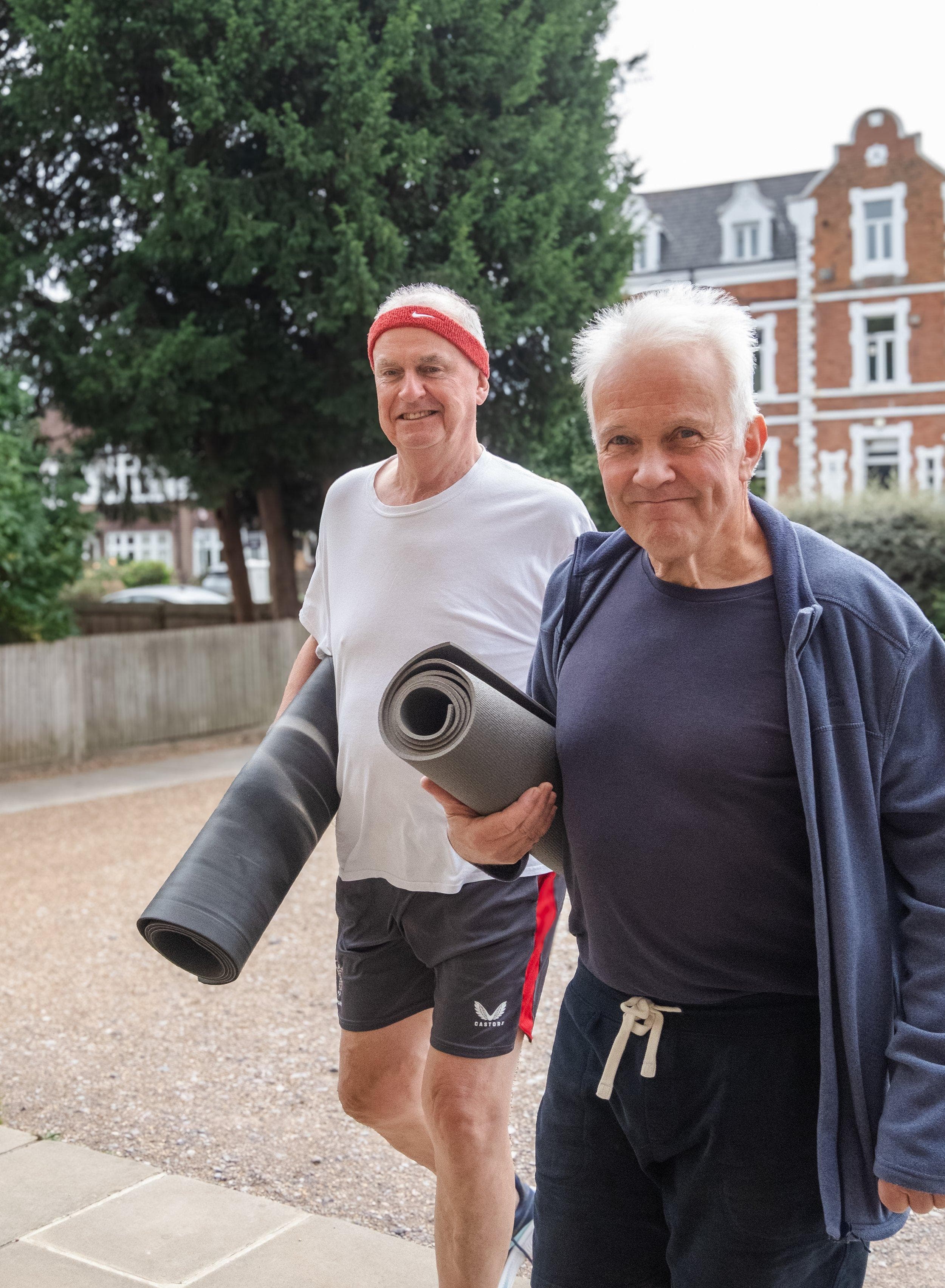 Two Welcome Pilates members walking to class carrying rolled mats